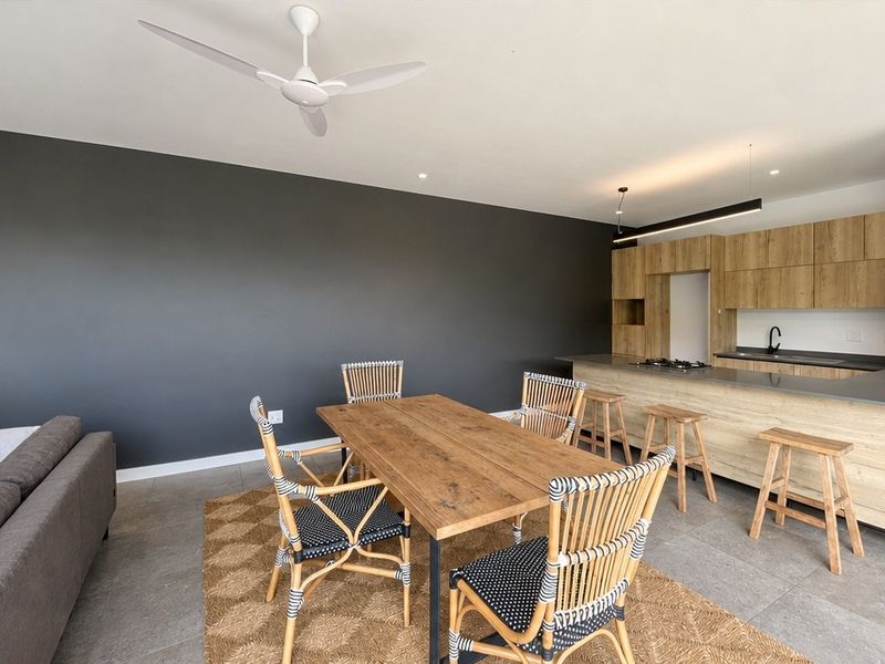 Modern open-plan living and dining area featuring a contemporary kitchen with wood-finish cabinetry, a central island, and sleek tiled flooring.