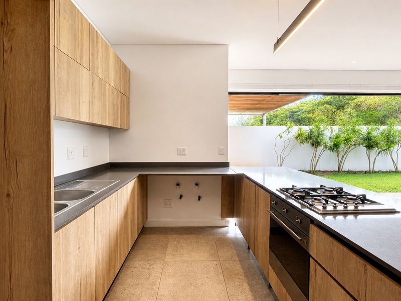 Modern kitchen featuring light wood cabinetry, stone countertops, integrated gas hob, and oven, with seamless flow to the outdoor patio area.