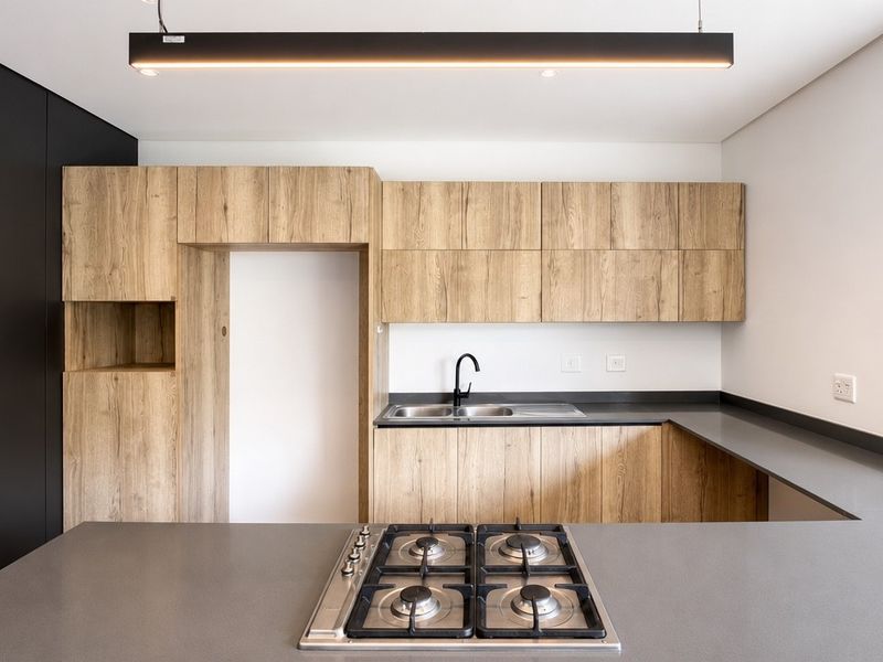 Modern kitchen featuring wood-grain cabinetry, dark stone countertops, a built-in gas hob, and a sleek black mixer tap with a minimalist pendant light.