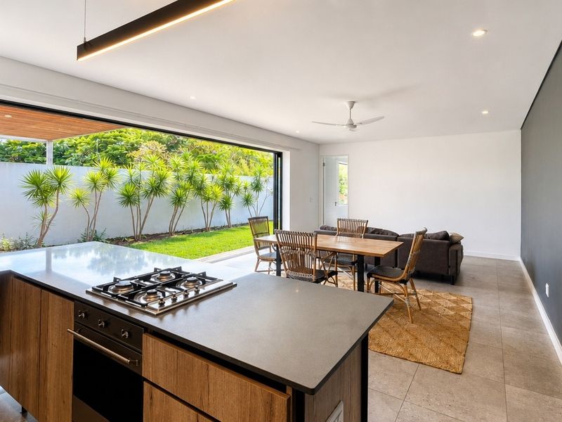 Modern open-plan kitchen and living area featuring a central island with gas cooktop, sleek cabinetry, and large sliding doors opening to a private garden.