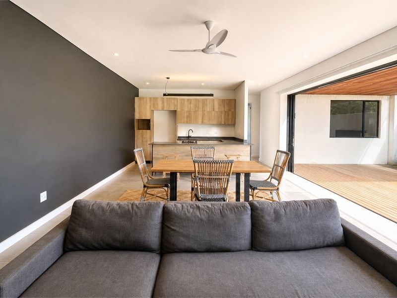 Modern open-plan living and kitchen area featuring sleek cabinetry, a central island, and seamless flow to an outdoor timber deck through large sliding doors.