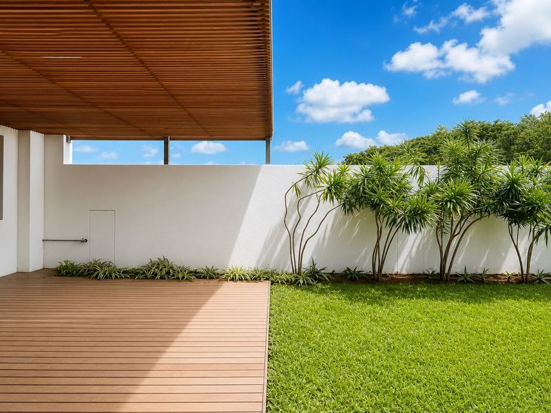 A modern outdoor patio featuring timber decking and a slatted pergola, overlooking a well-maintained private garden with a boundary wall.