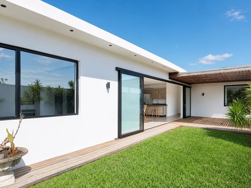 A modern rear exterior featuring a timber deck, manicured lawn, and large sliding glass doors providing seamless indoor-outdoor flow.