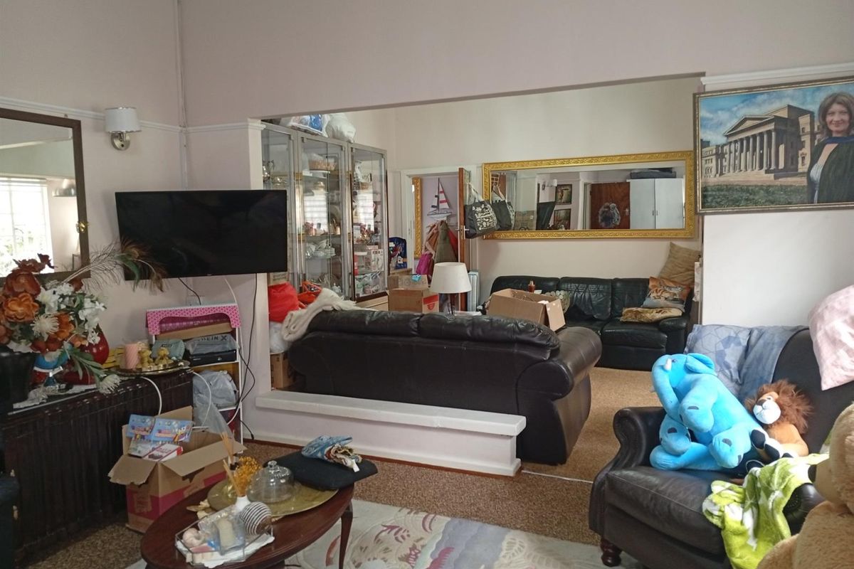 A spacious living area featuring a large wall-mounted television, built-in display cabinetry, and a wide opening connecting to an adjacent room.