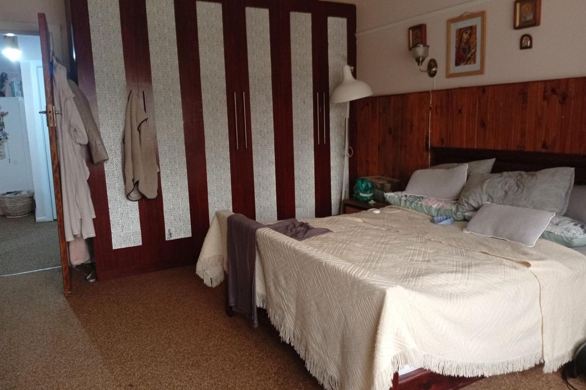 A bedroom featuring built-in wardrobes, wood wall paneling, and carpet flooring, offering a dated aesthetic with potential for modernization.