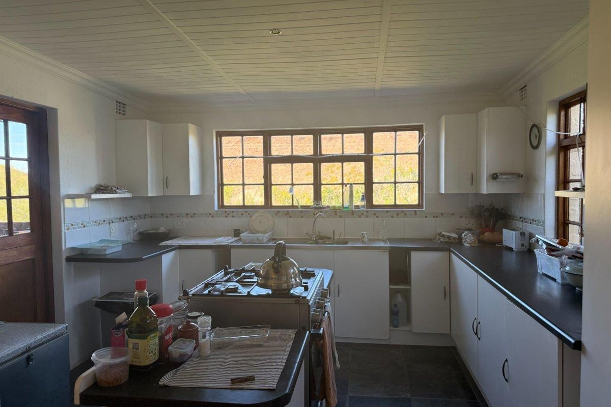 A functional kitchen featuring white cabinetry, dark countertops, a central gas stove, and a large window overlooking the surrounding landscape.