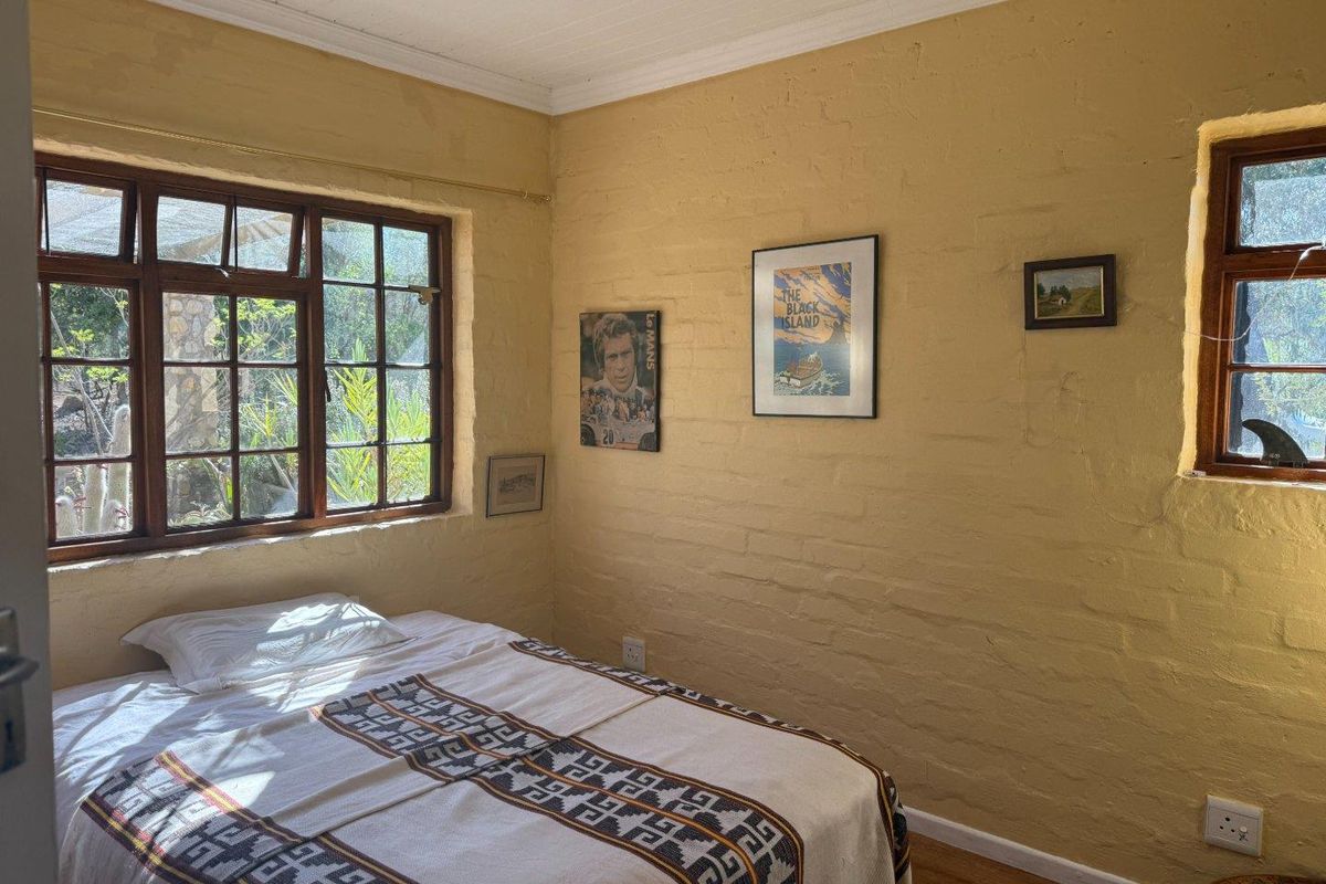 A cozy bedroom featuring rustic painted brick walls, timber-framed windows, and wooden flooring, offering a warm and characterful living space.