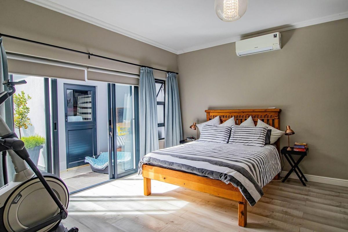 A well-maintained bedroom featuring light wood-look flooring, neutral walls, a wall-mounted air conditioning unit, and large sliding glass doors opening to a patio.