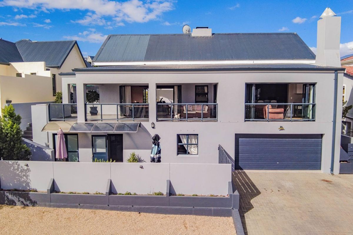 A modern two-story residential exterior featuring a spacious upper-level balcony, a paved driveway, and an integrated garage.