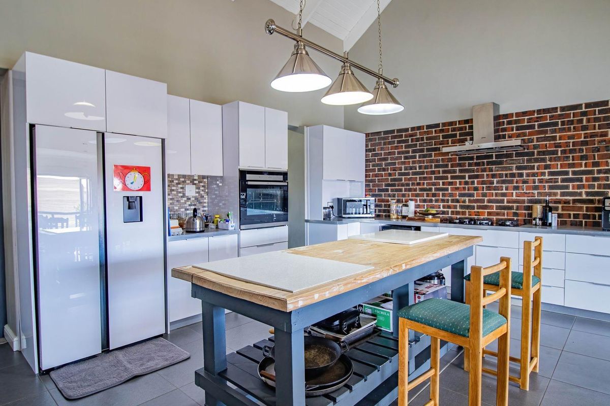 Modern kitchen featuring high-gloss white cabinetry, a central island with a wooden countertop, exposed brick feature wall, and stainless steel extractor fan.