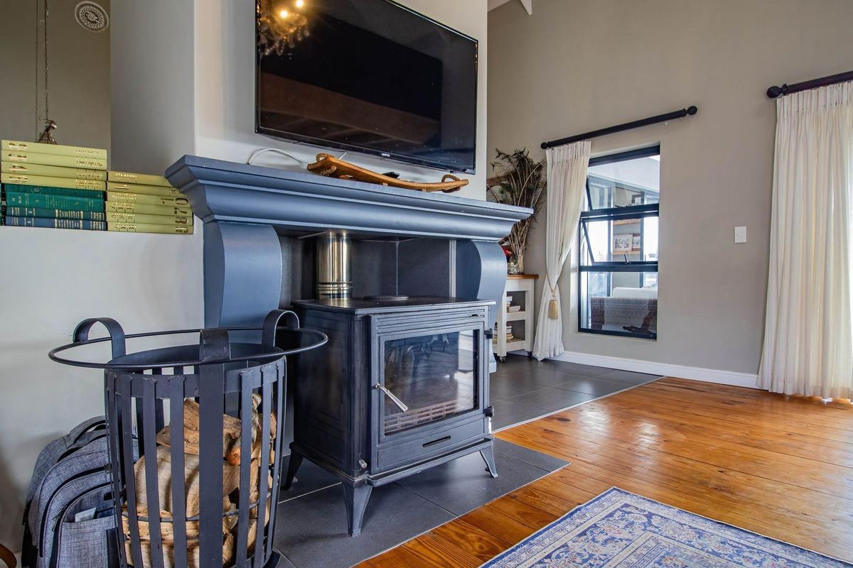 A cozy living room featuring a prominent dark-painted fireplace mantel with a built-in wood-burning stove, set against a backdrop of hardwood flooring.