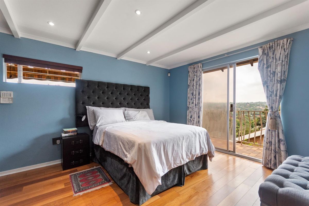 Spacious bedroom featuring hardwood flooring, exposed ceiling beams, recessed lighting, and sliding glass doors providing direct access to a private balcony with scenic views.