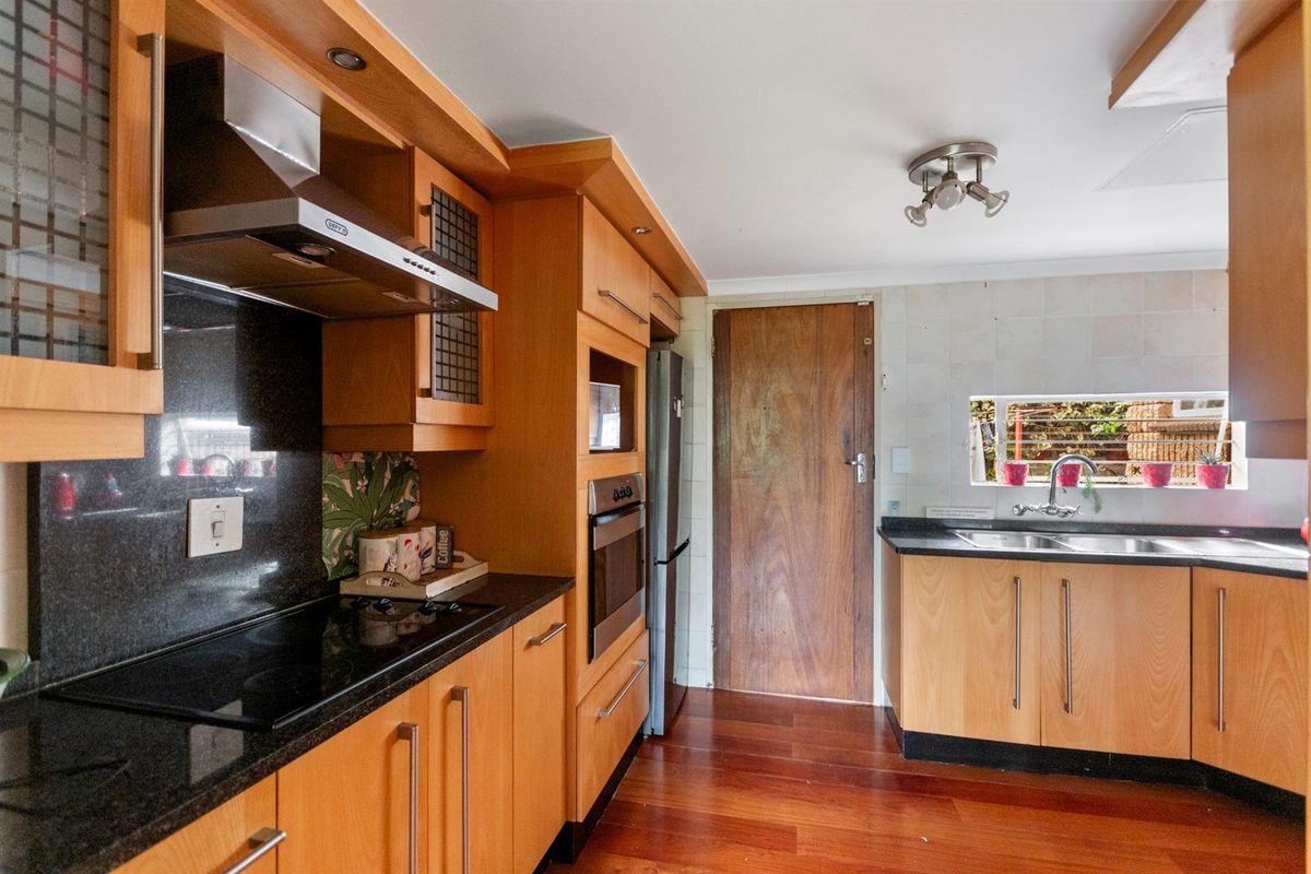 A functional kitchen featuring wooden cabinetry, granite countertops, built-in oven, electric hob, and hardwood flooring, offering a classic and practical layout.