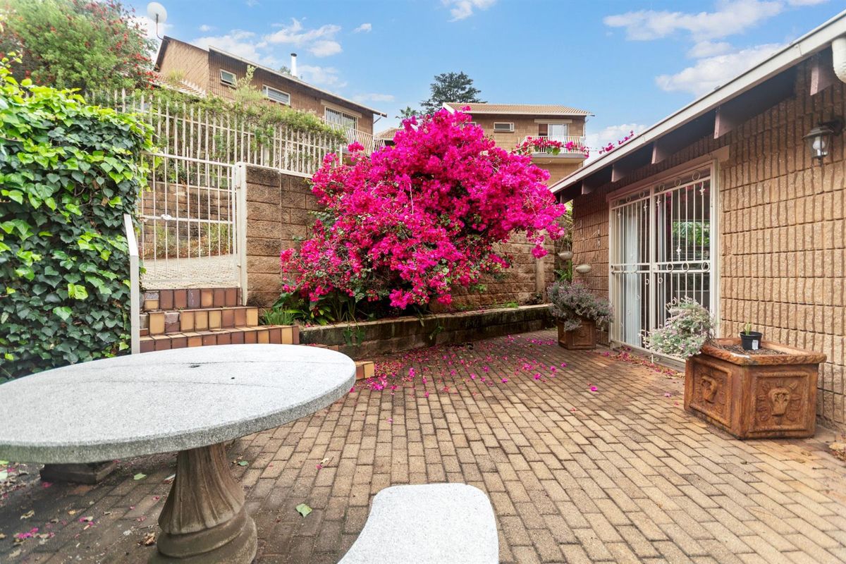 A private rear courtyard featuring brick paving, a retaining wall with mature bougainvillea, and secure access to the townhouse interior.