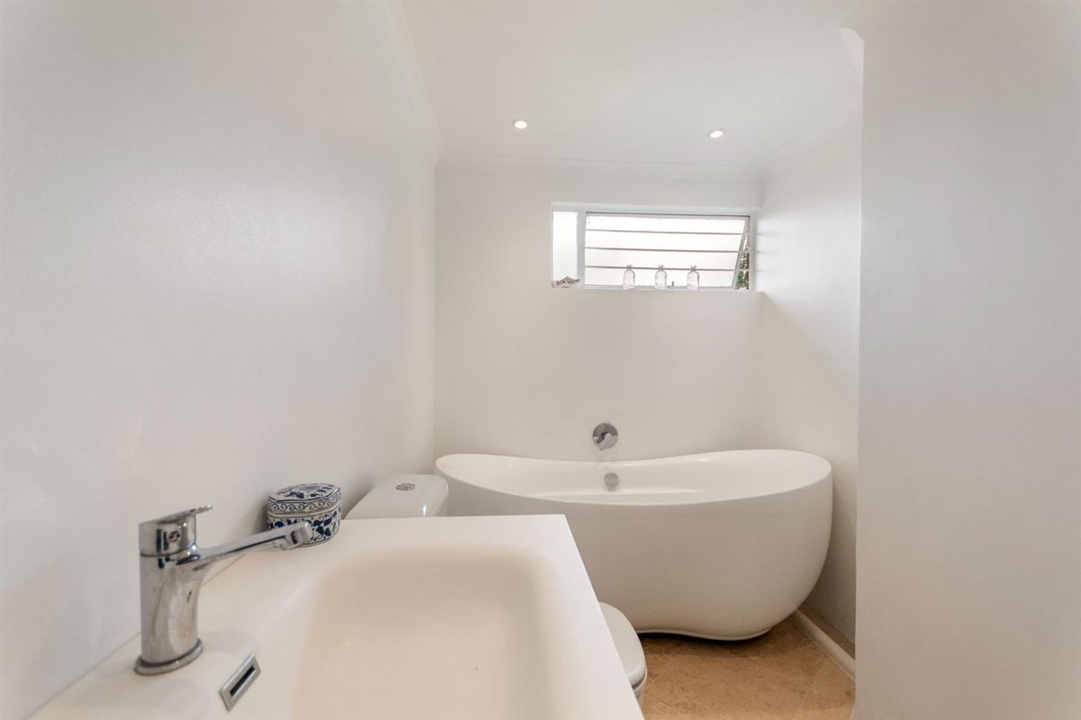 A clean and modern bathroom featuring a sleek freestanding bathtub, a vanity basin with chrome fixtures, and natural light from a louver window.