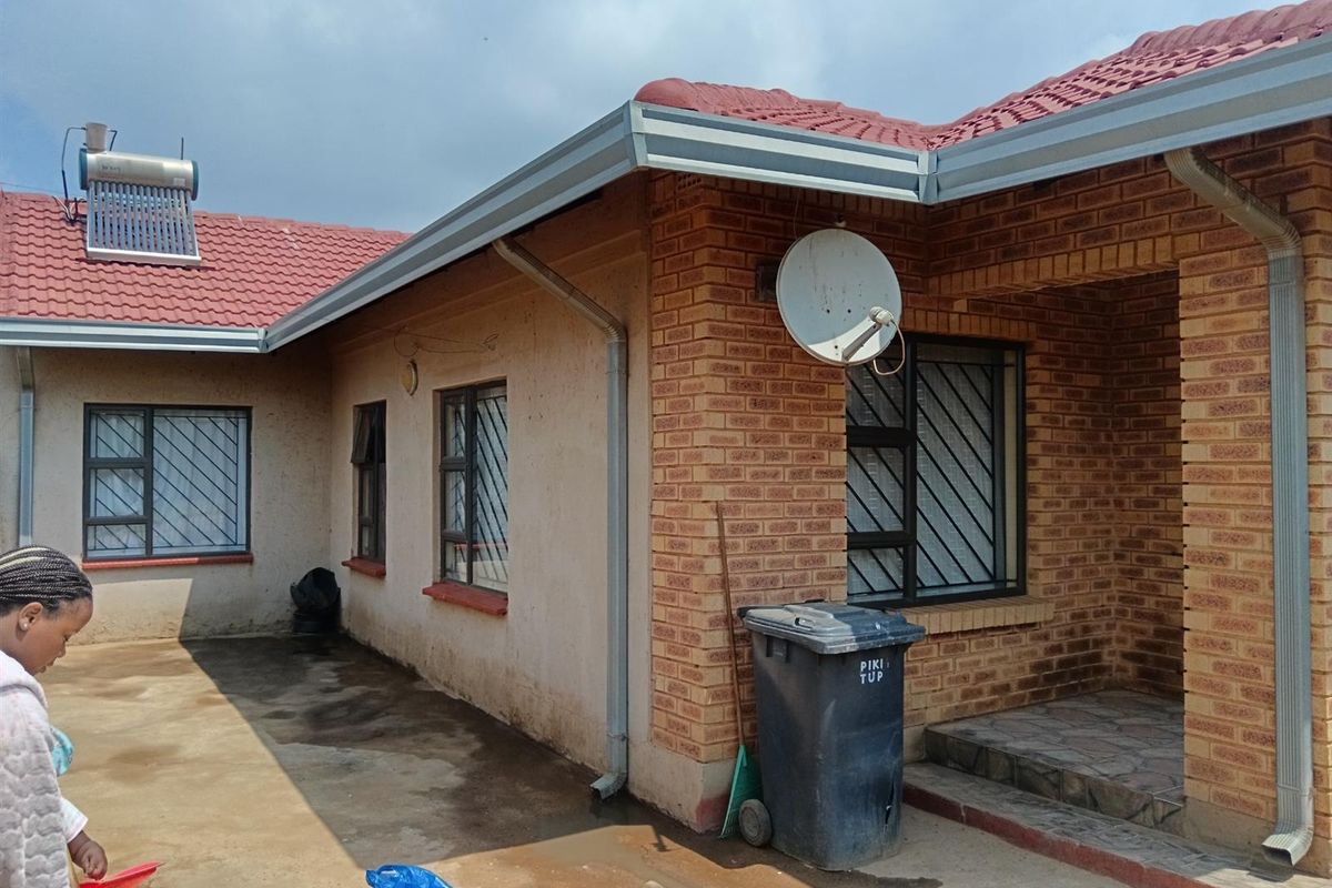 Exterior view of the house featuring face brick and plastered walls, red tiled roof, solar water heater, and security bars on windows.