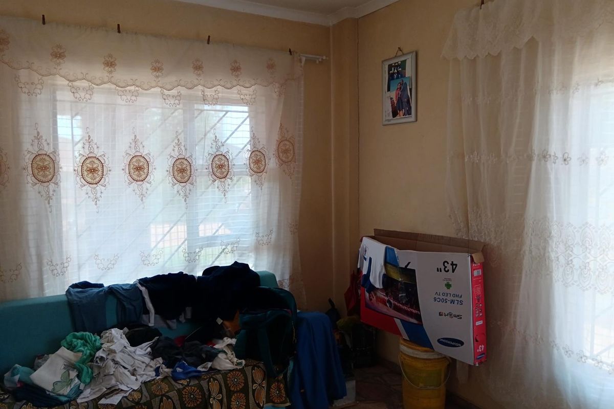 A living room area featuring large windows with curtains and tiled flooring, offering a functional space with potential for cosmetic updates.
