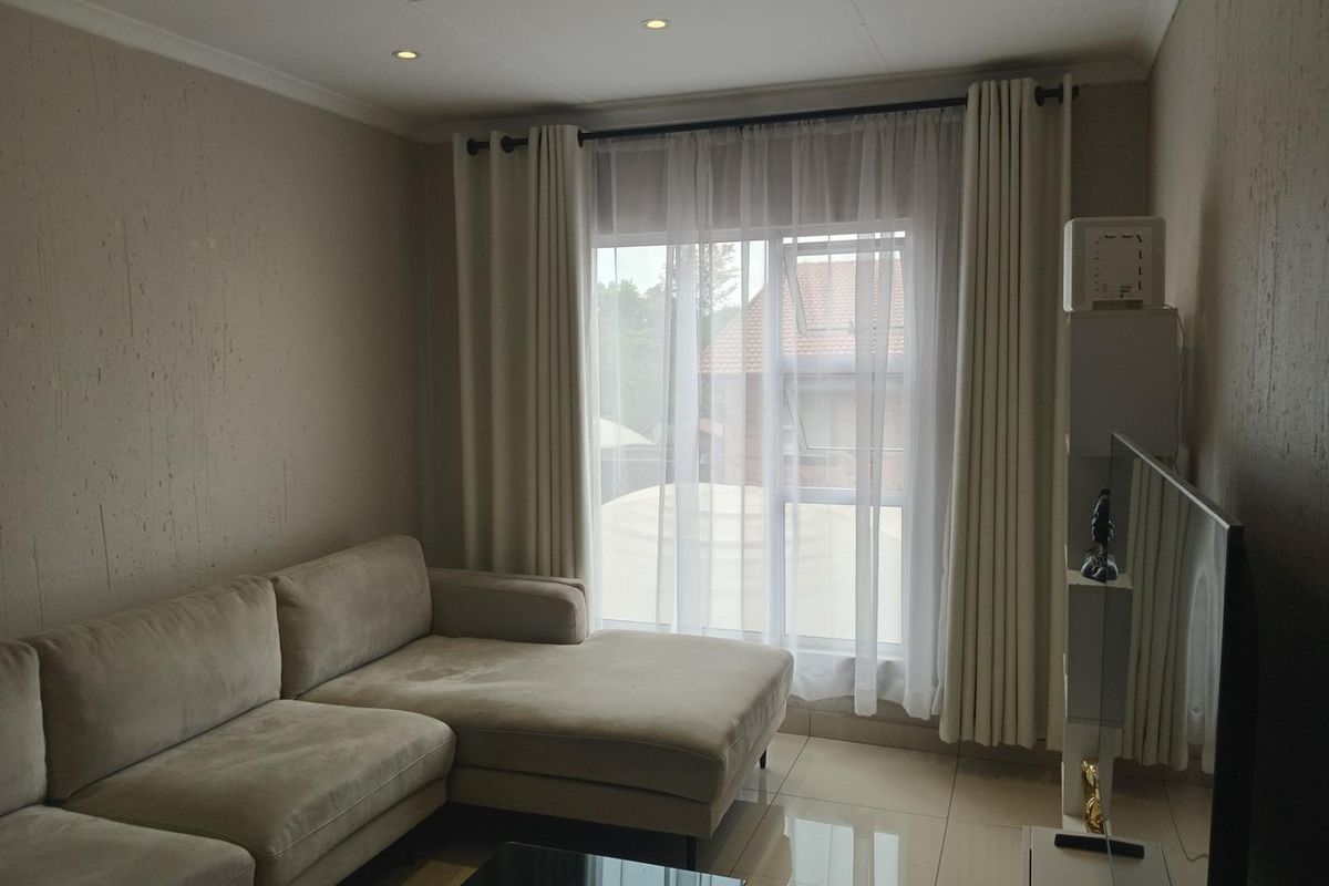 A well-maintained living room featuring neutral textured walls, polished tiled flooring, and recessed downlighting, creating a bright and comfortable living space.