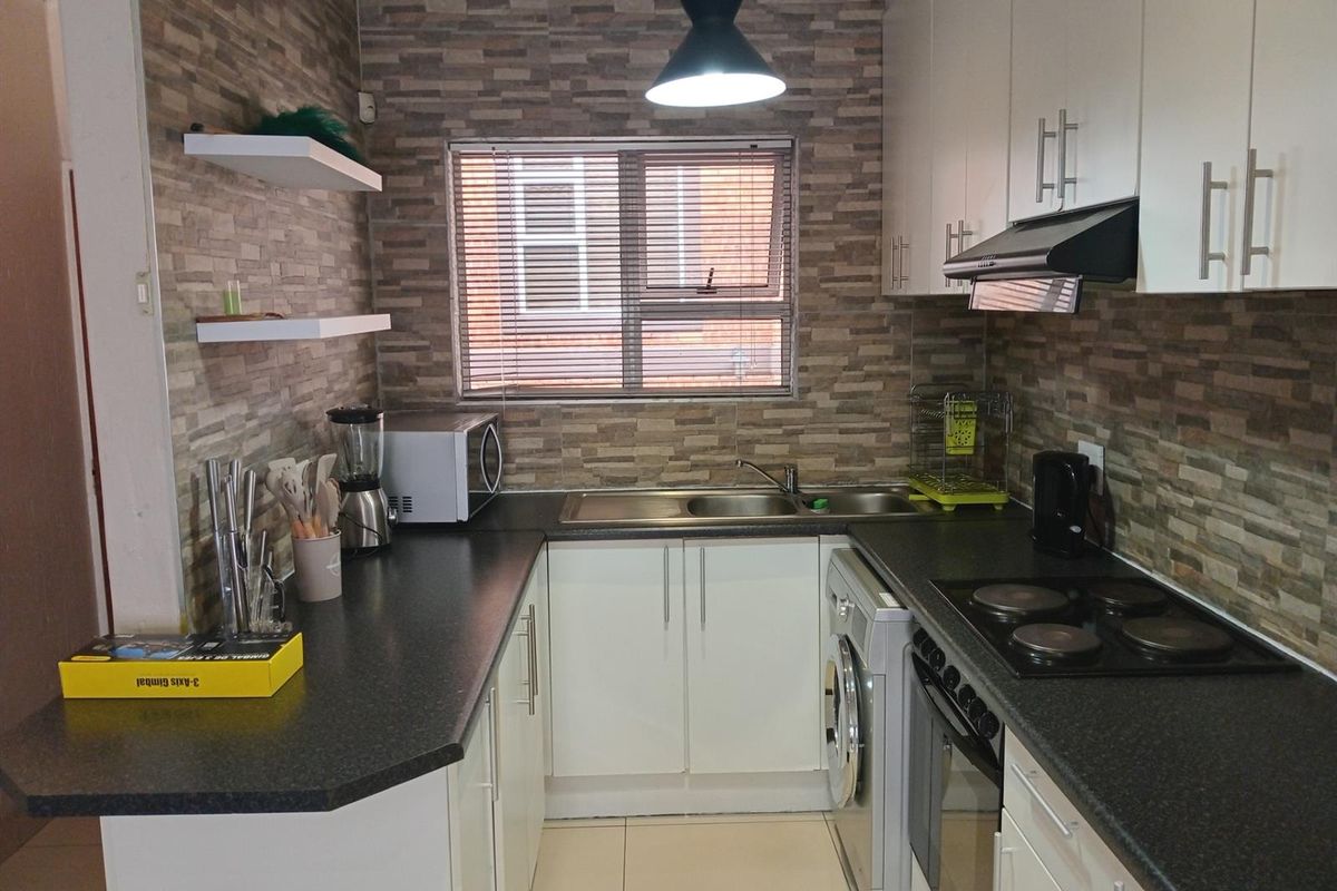 A functional kitchen featuring white cabinetry, dark laminate countertops, a built-in oven with hob, and decorative stone-look wall cladding.