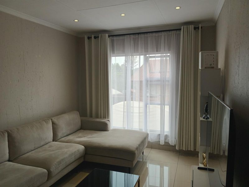 A well-maintained living room featuring neutral textured walls, polished tiled flooring, and recessed downlighting, creating a bright and comfortable living space.