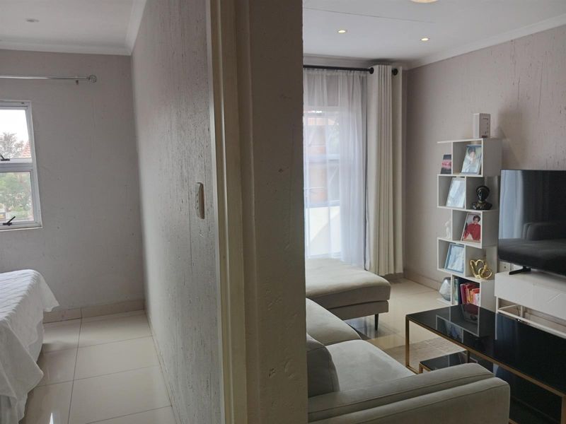 An open-plan living area and bedroom space featuring neutral tiled flooring, recessed lighting, and large windows allowing for natural light.