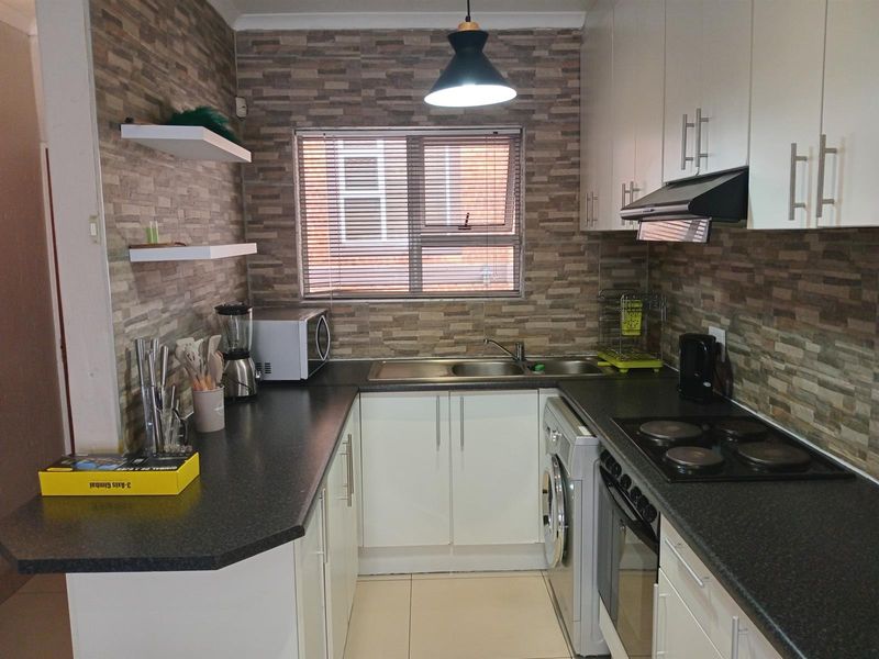 A functional kitchen featuring white cabinetry, dark laminate countertops, a built-in oven with hob, and a dedicated space for a washing machine.