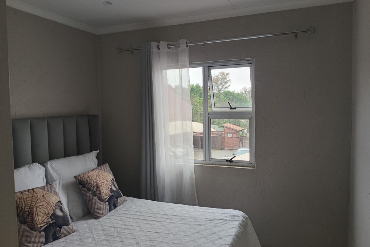 A bedroom featuring neutral walls, an aluminium window frame, and recessed ceiling lighting, offering a functional space with potential for cosmetic updates.