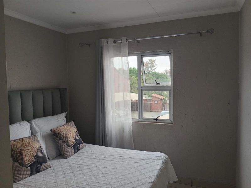 A bedroom featuring neutral walls, an aluminium window frame, and recessed ceiling lighting, offering a functional space with potential for cosmetic updates.