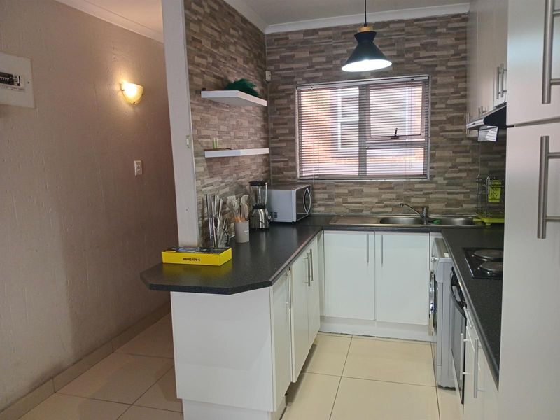 A functional kitchen featuring white cabinetry, dark laminate countertops, stone-look feature wall, and integrated appliances, offering a clean and practical workspace.