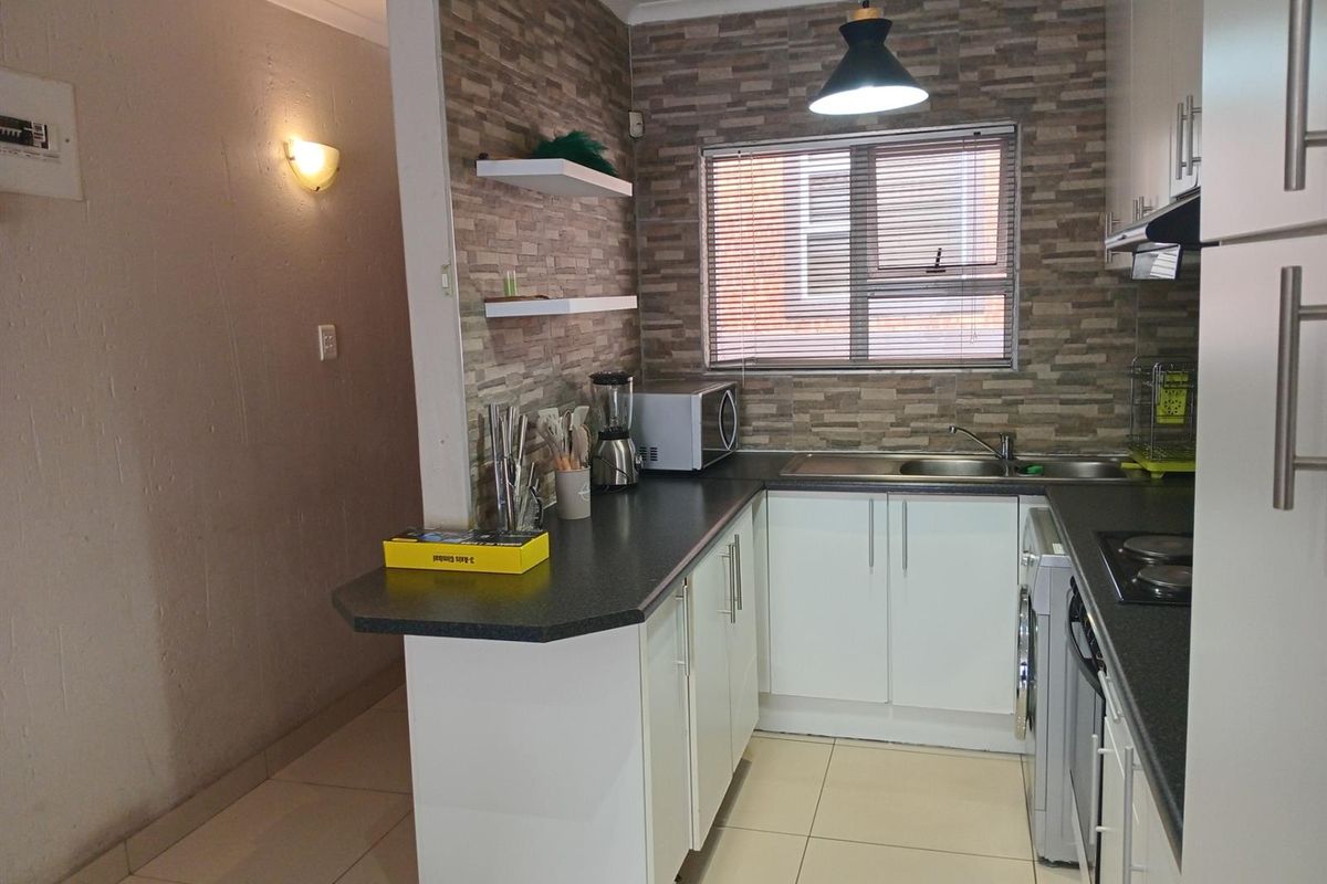A functional kitchen featuring white cabinetry, dark laminate countertops, stone-look feature wall, and integrated appliances, offering a clean and practical workspace.