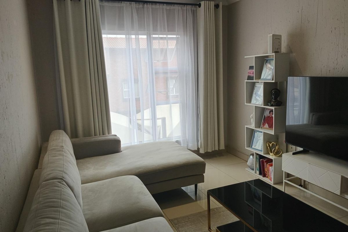 A well-maintained living room featuring neutral tiled flooring and a large sliding glass door that provides natural light.