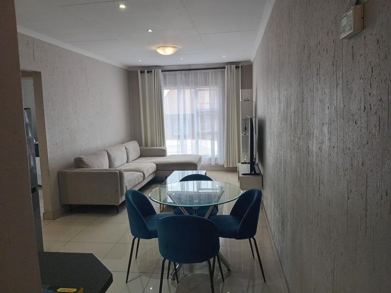 An open-plan living and dining area featuring neutral tiled flooring, textured wall finishes, and recessed lighting, creating a bright and functional living space.