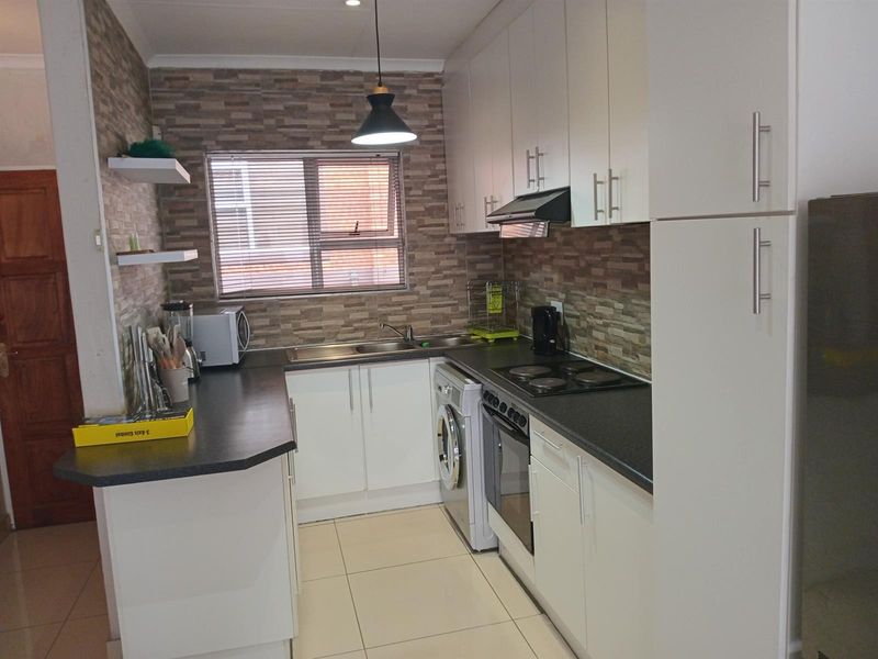 Compact kitchen featuring white cabinetry, dark laminate countertops, tiled backsplash, built-in oven, electric hob, and integrated laundry appliance space.