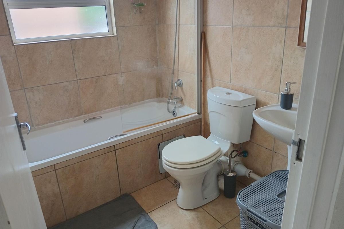 A functional bathroom featuring a bathtub with a glass screen, pedestal basin, and toilet, finished with neutral wall and floor tiling.