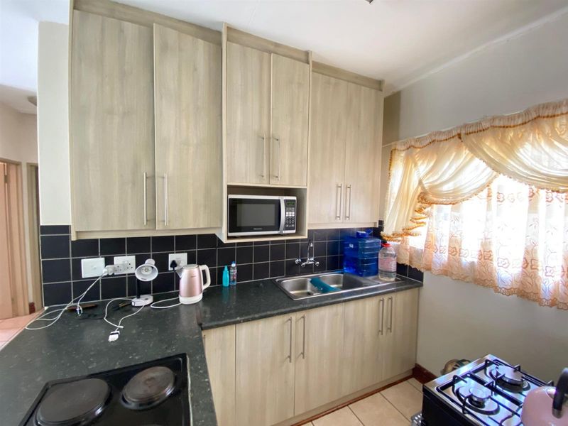 A functional kitchen featuring light wood-finish cabinetry, dark countertops, a tiled backsplash, and integrated appliances including a microwave and electric hob.