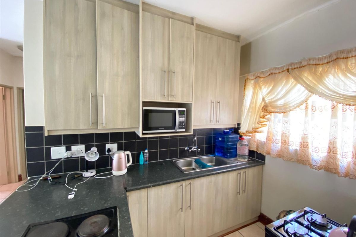A functional kitchen featuring light wood-finish cabinetry, dark countertops, a tiled backsplash, and integrated appliances including a microwave and electric hob.