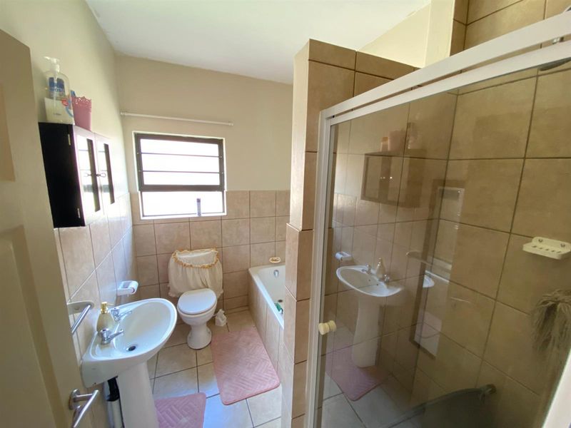 A functional bathroom featuring a pedestal basin, toilet, bathtub, and a separate glass-enclosed shower with neutral ceramic tiling throughout.