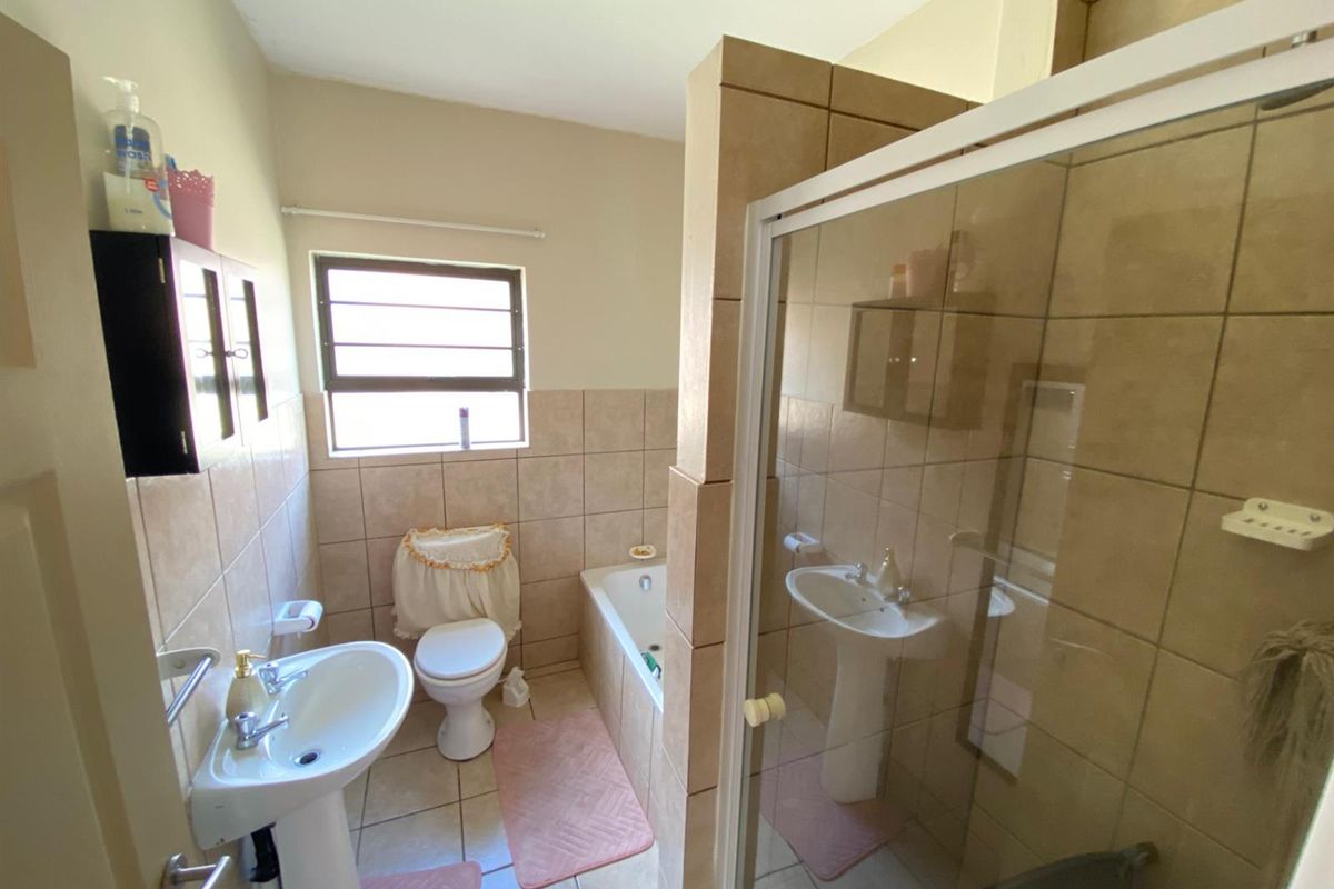A functional bathroom featuring a pedestal basin, toilet, bathtub, and a separate glass-enclosed shower with neutral ceramic tiling throughout.