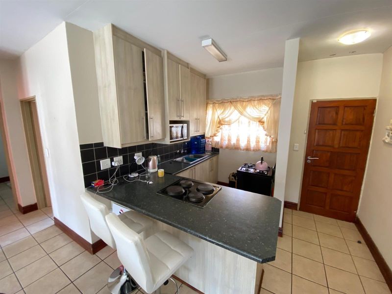 Compact kitchen featuring light wood-look cabinetry, dark laminate countertops, a black tile backsplash, and a functional electric hob with breakfast bar seating.