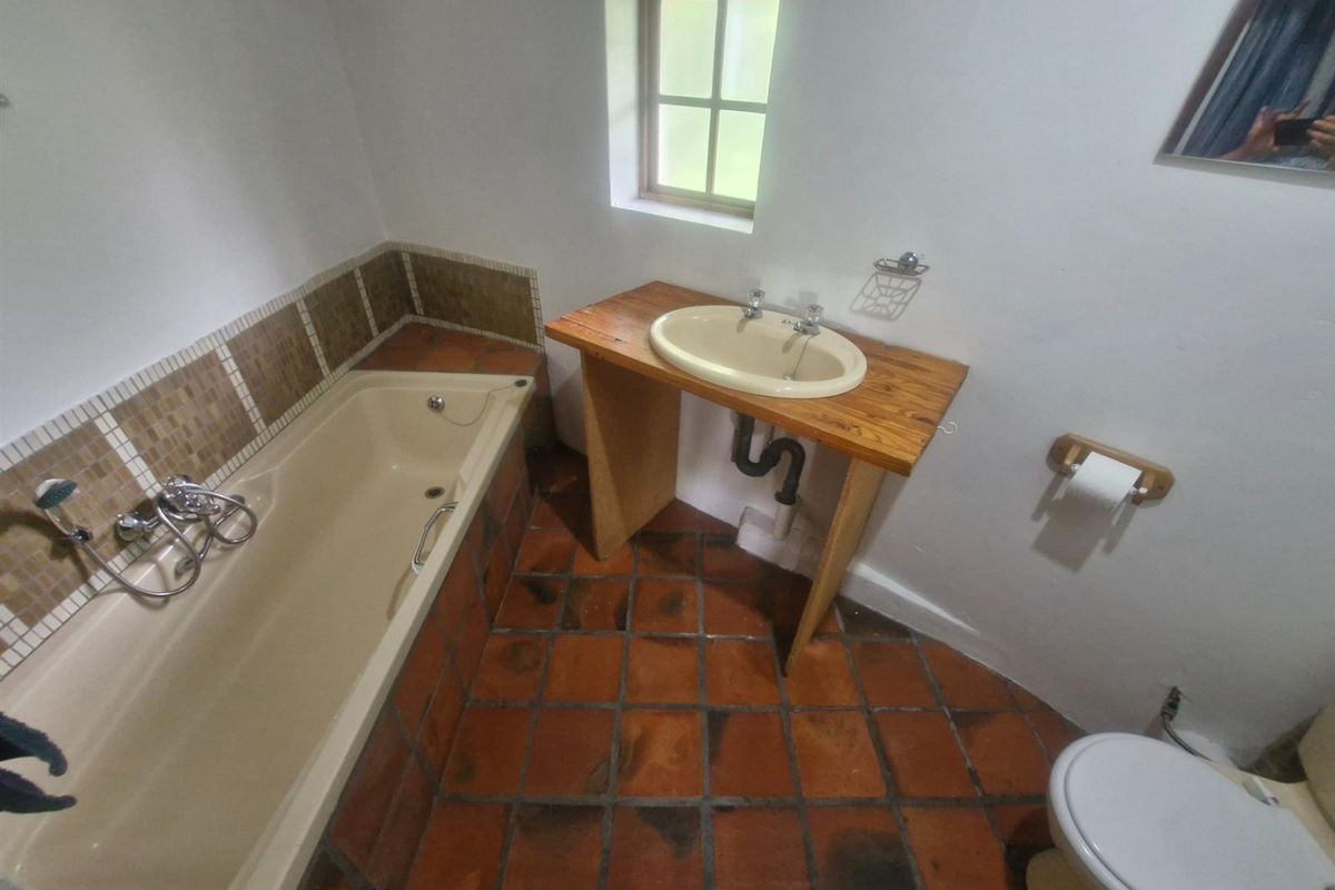A functional bathroom featuring a built-in bathtub with mosaic tile surround, a pedestal-style vanity with basin, and terracotta floor tiles.