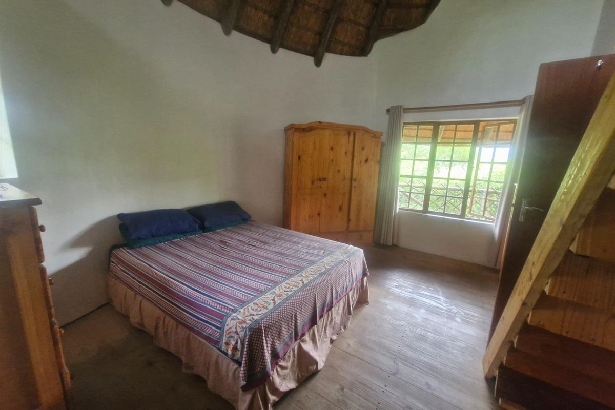 A rustic bedroom featuring a high thatched ceiling, timber flooring, and large windows providing natural light.