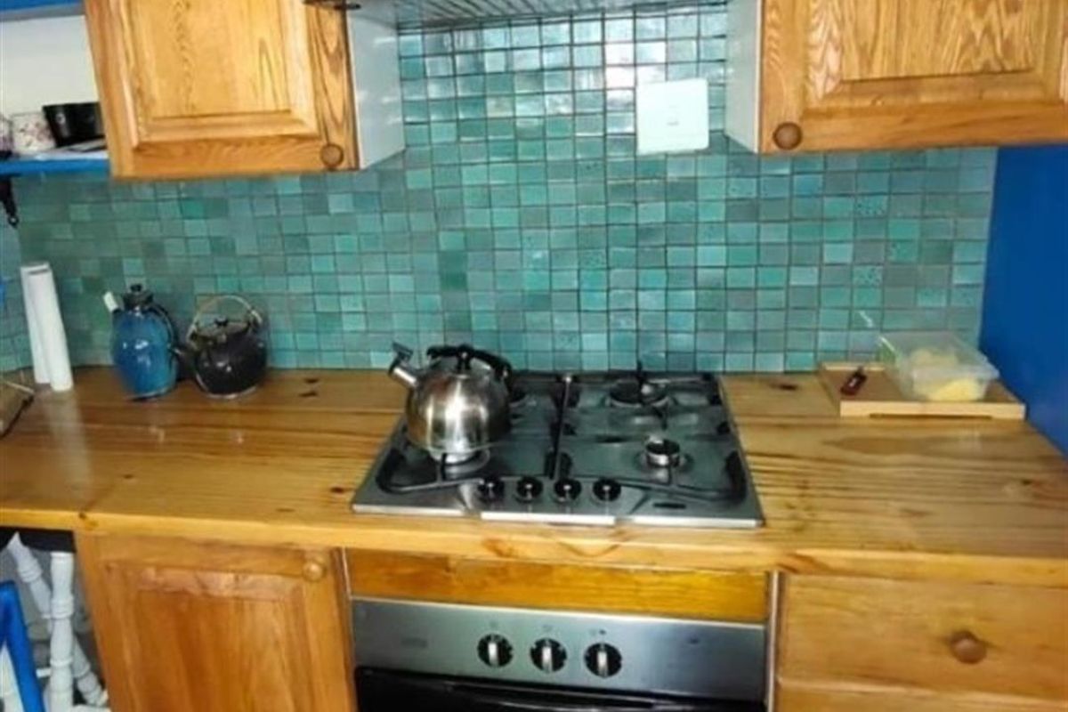 A kitchen workspace featuring timber cabinetry, a gas hob, built-in oven, stainless steel extractor fan, and a decorative green mosaic tile splashback.