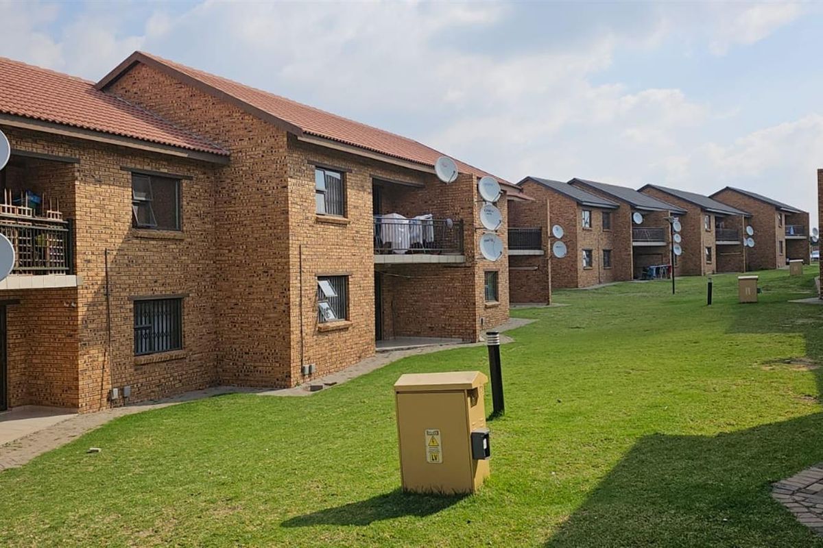 Exterior view of a multi-story brick apartment complex featuring communal green spaces, balconies, and satellite dish installations.