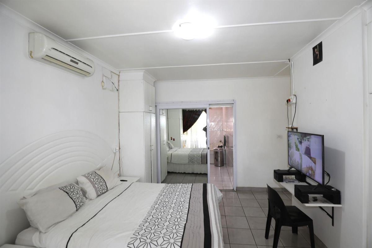 A bedroom featuring tiled flooring, built-in cupboards, and a wall-mounted air conditioning unit, with an adjoining en-suite bathroom visible through a sliding door.