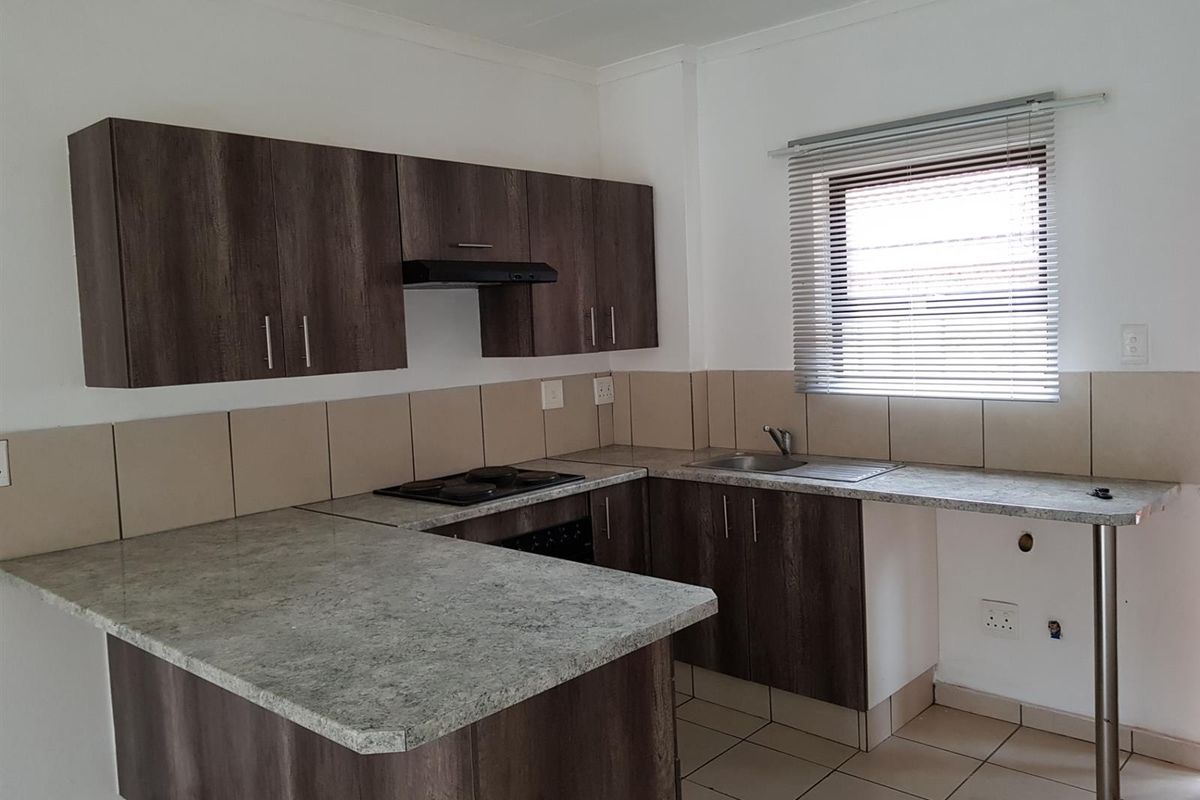 A functional kitchen featuring dark wood-look cabinetry, stone-effect countertops, a built-in hob, extractor fan, and tiled splashbacks with a window for natural light.