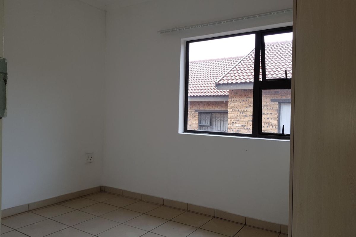 A vacant bedroom featuring neutral tiled flooring, white walls, and a large window providing natural light and a view of the neighboring property.