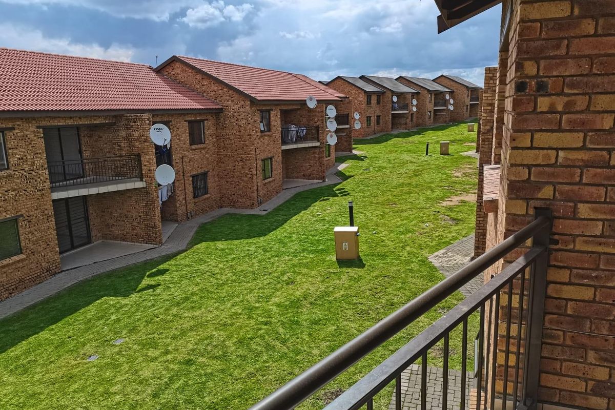 View of the apartment complex grounds featuring face-brick buildings, manicured lawns, paved walkways, and private balconies.