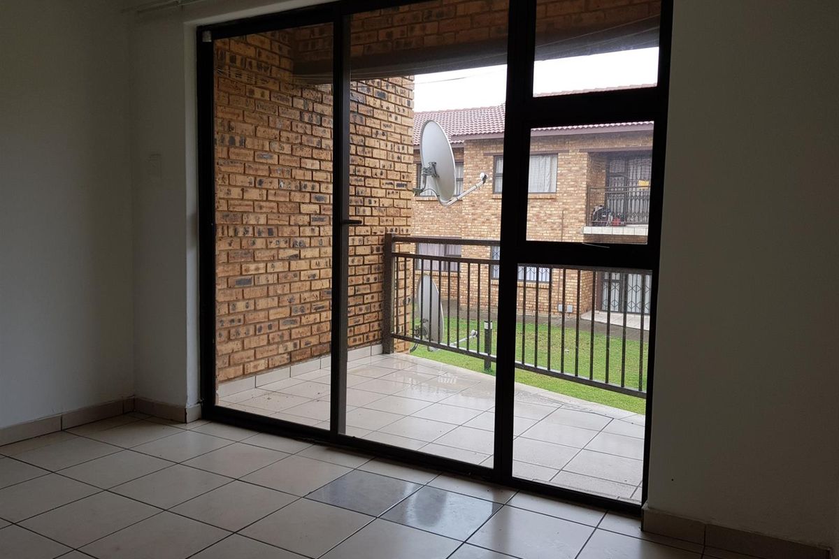 Interior view of a living area featuring large sliding glass doors that open onto a tiled balcony with brick wall detailing.