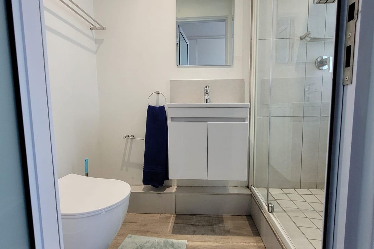 Modern bathroom featuring a wall-mounted vanity, glass-enclosed shower, and neutral finishes. Note visible ceiling staining requiring attention.