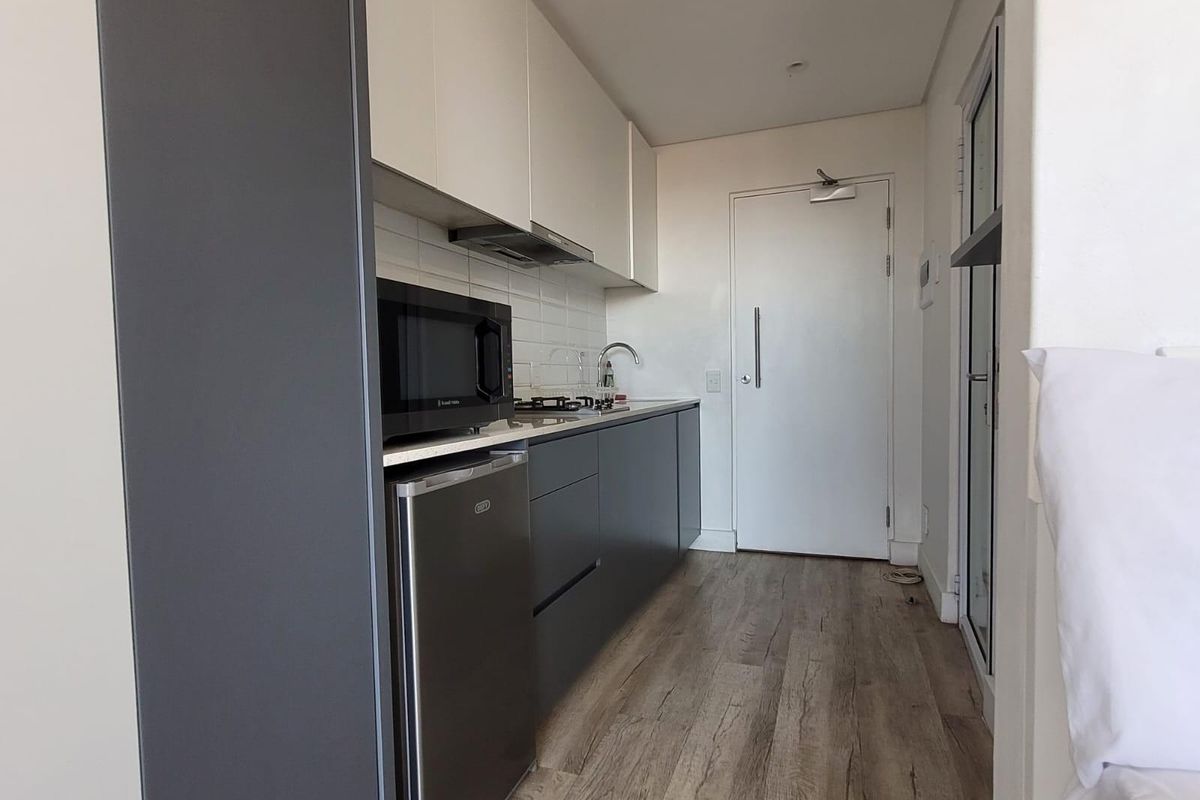 A modern, compact kitchen featuring two-tone cabinetry, a gas hob, extractor fan, built-in microwave, and durable laminate flooring.